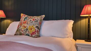 A neatly made bed with a colorful floral pillow, white linens, and two bedside lamps.