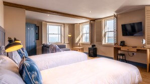 Een hotelkamer met twee bedden, een bureau, een televisie en uitzicht op zee.
