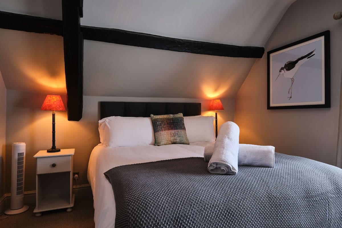 A neatly made bed with white linens, two bedside lamps, a small bedside table, and a framed picture on the wall.