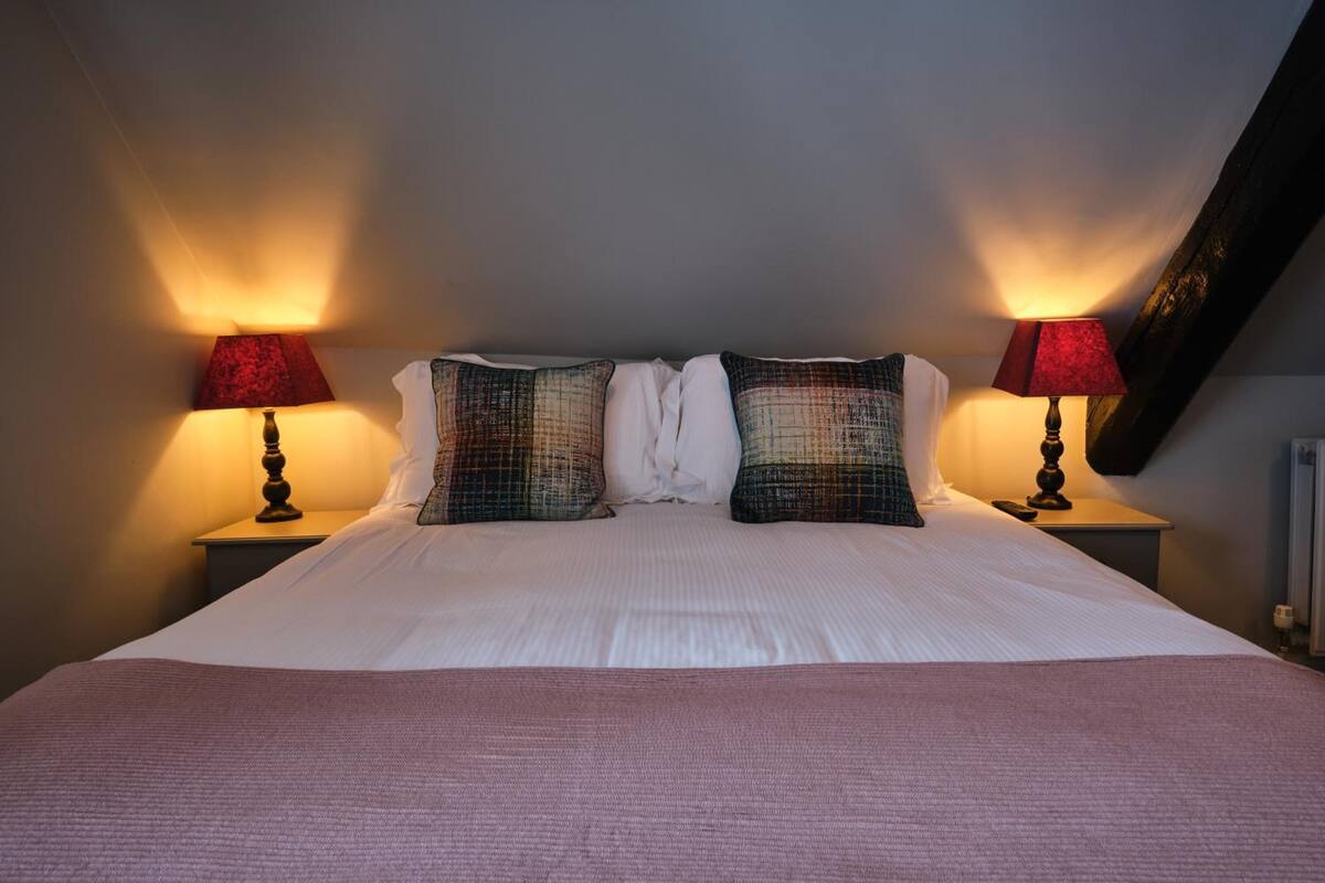 A neatly made bed with a white duvet and two pillows, flanked by two bedside tables with lamps.