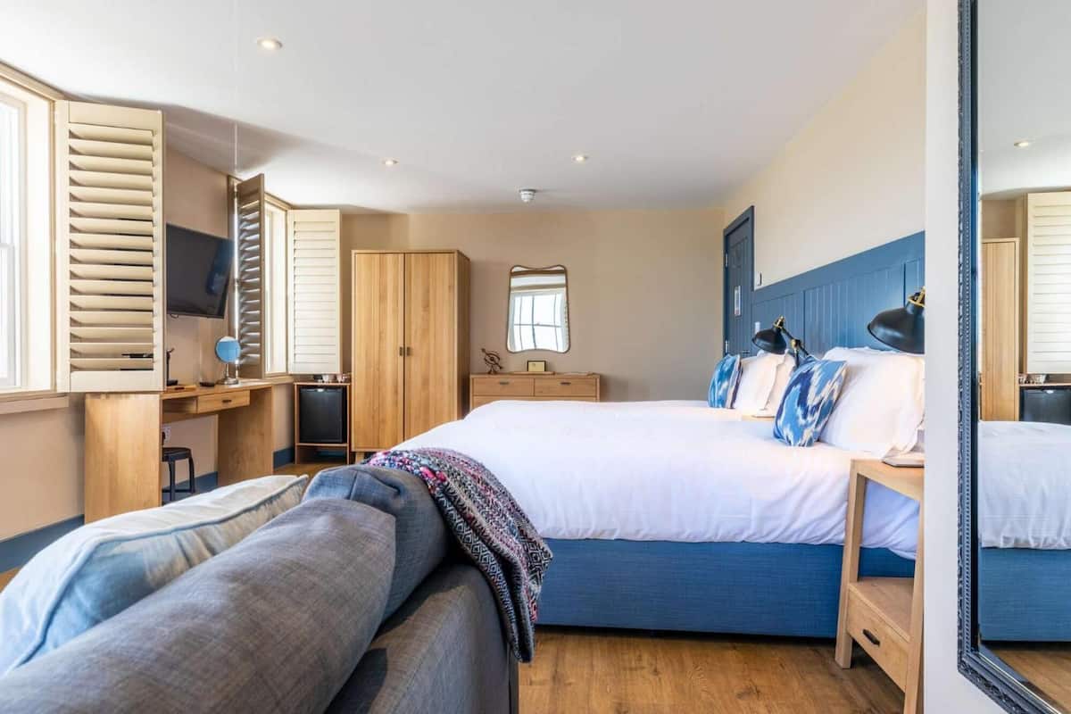 A bedroom with a bed, a desk, a wardrobe, a mirror, and a television.