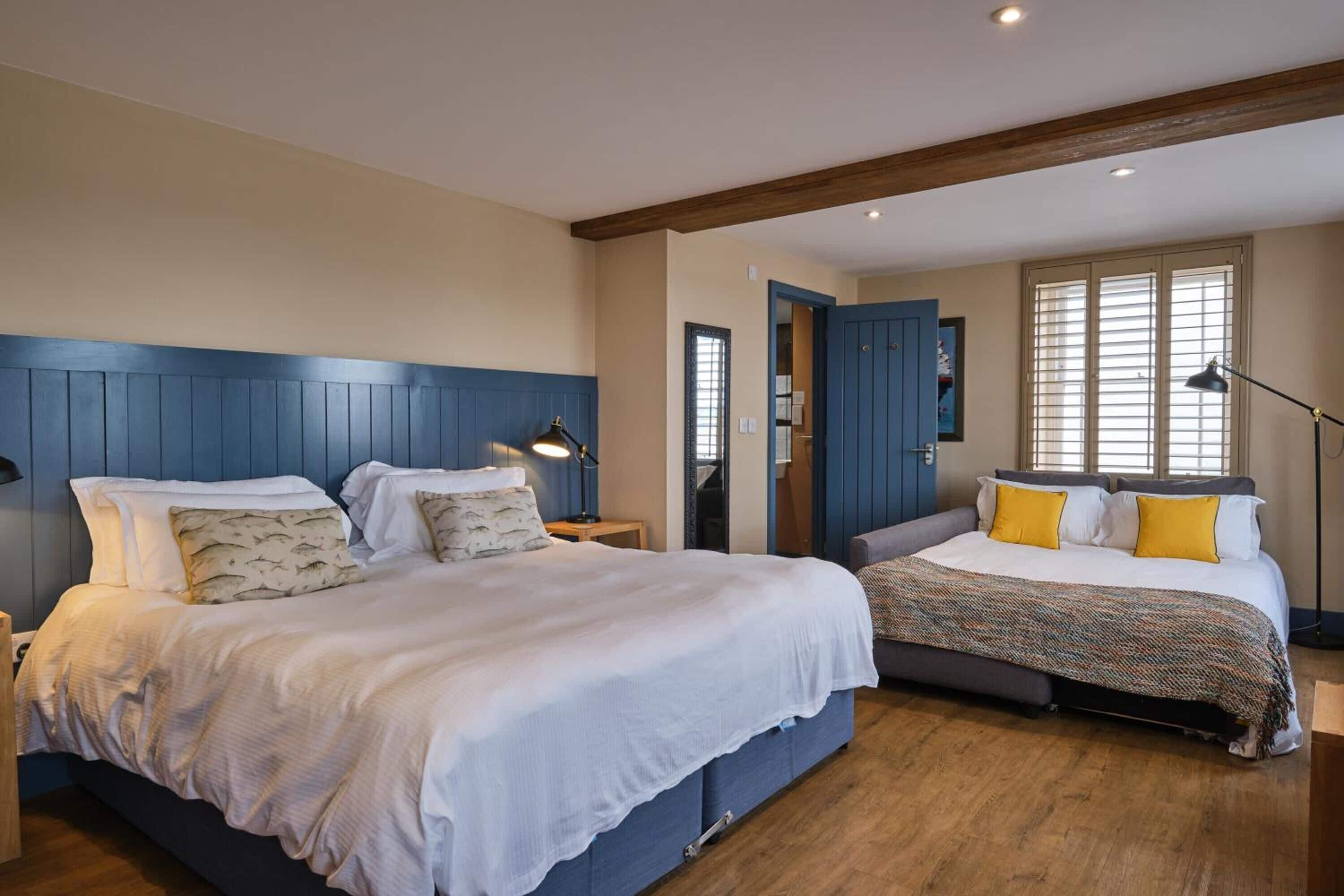 Une chambre avec deux lits, un plancher en bois et une tête de lit bleue.