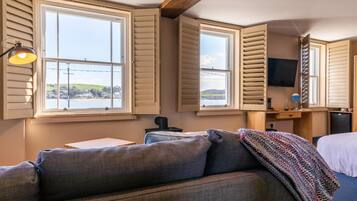 A room with a large window, a sofa, a desk, and a television.