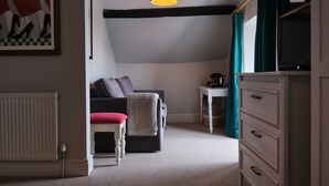 Een knus ingerichte kamer met een donkere bank, een tafeltje, een stoel en een televisie op een standaard.
