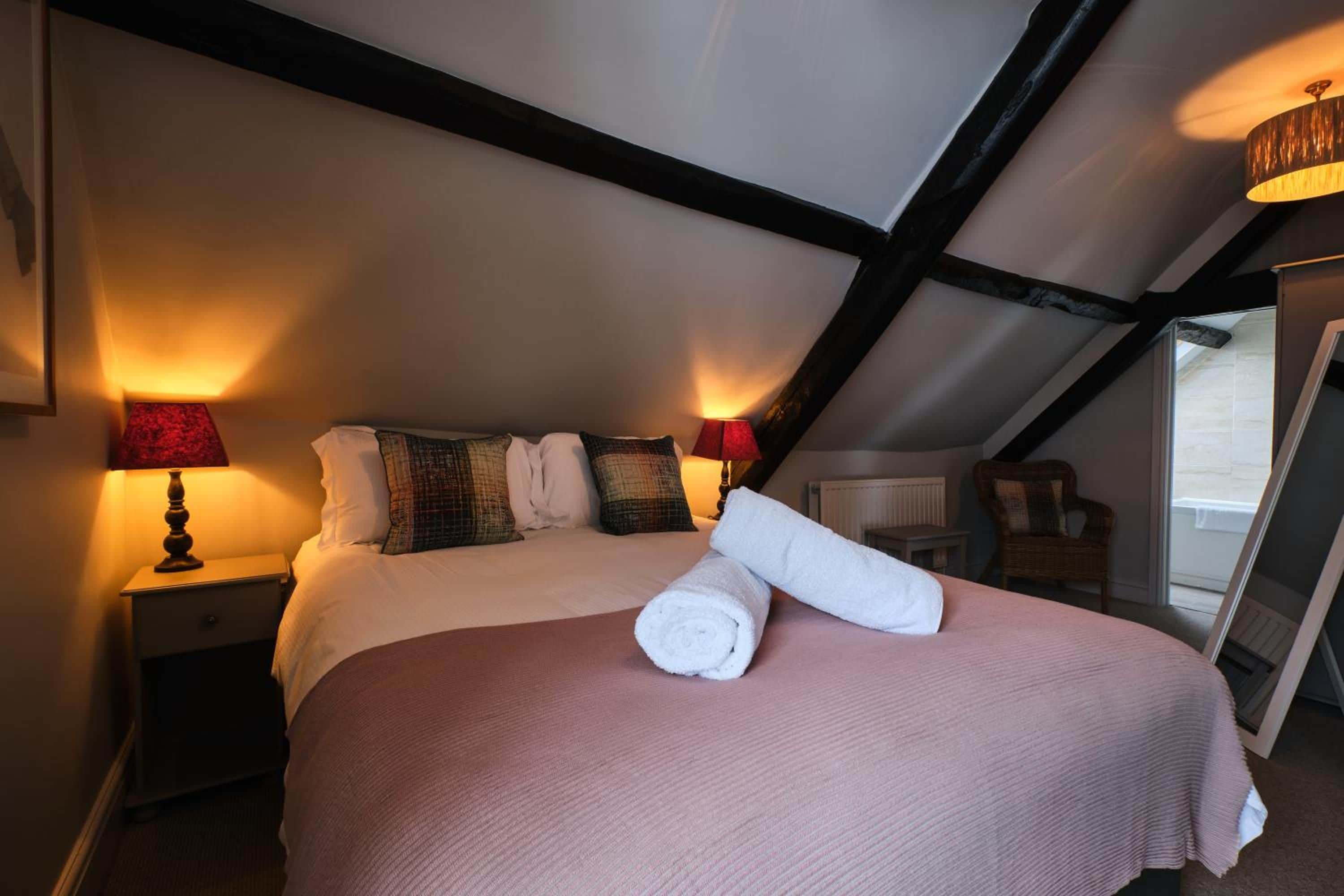 Ein Schlafzimmer mit einem großen Bett, zwei Nachttischlampen, einem zusammengerollten Handtuch und einem Spiegel.