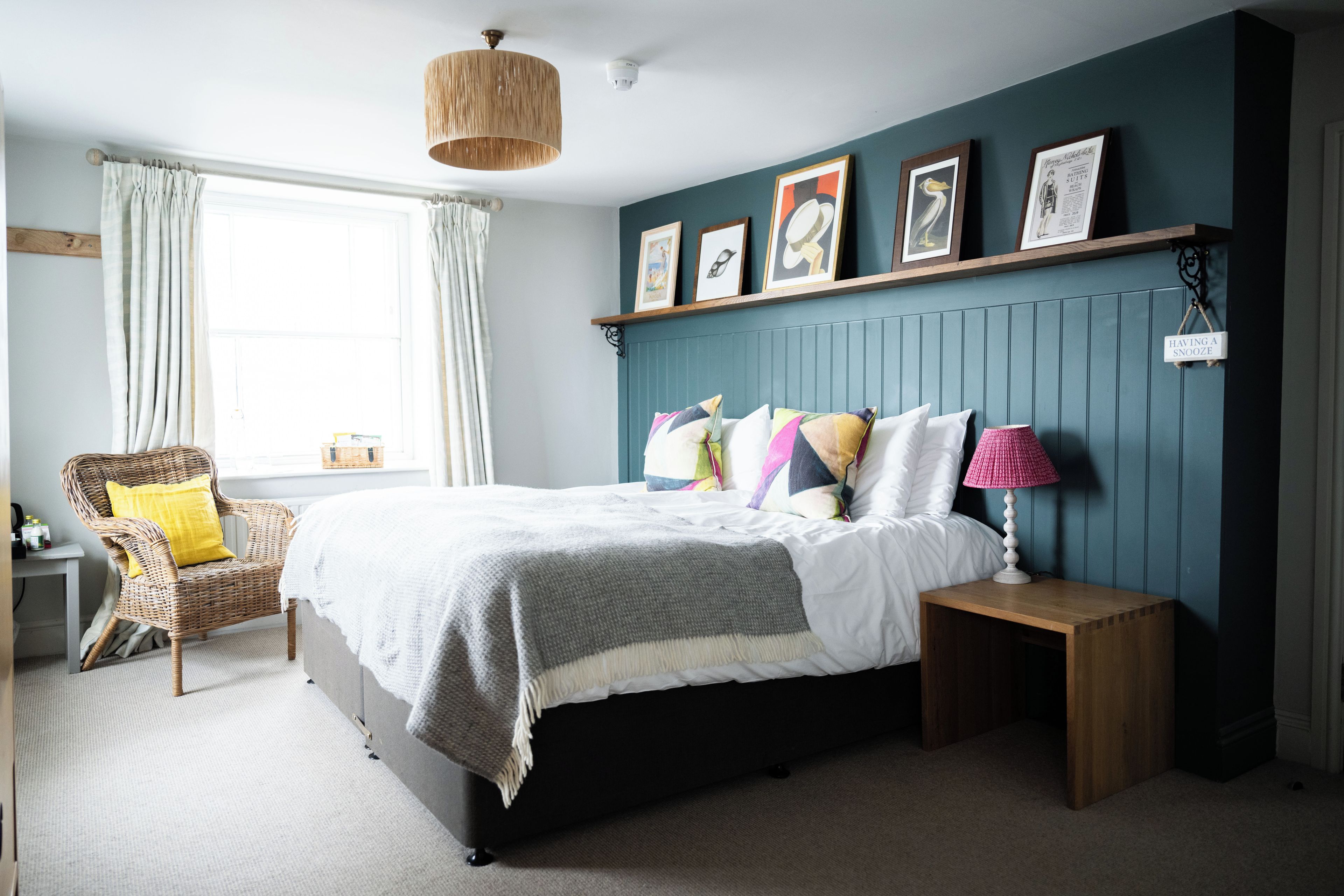 A bedroom with a bed, bedside table, lamp, chair, and a window with curtains.
