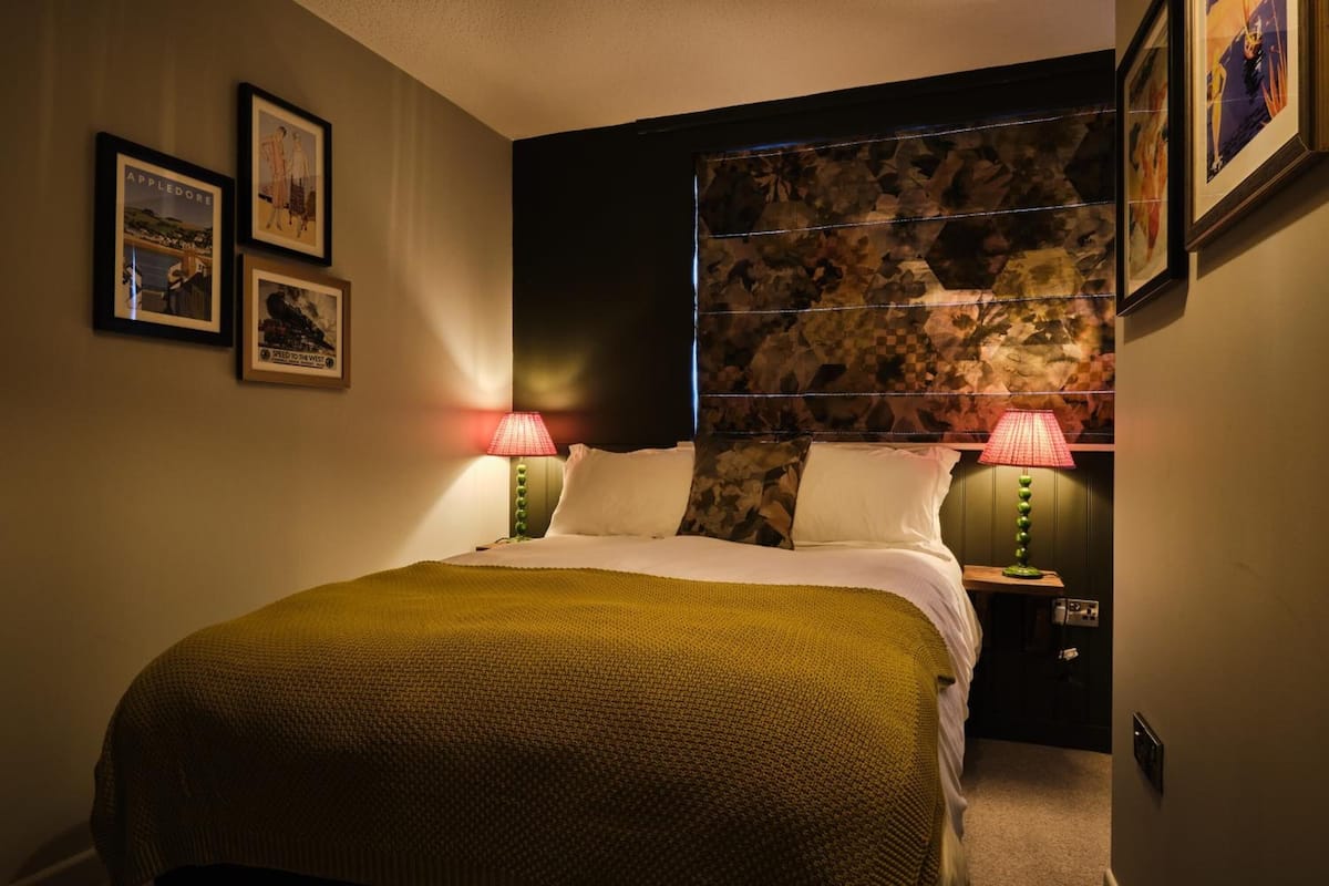 A bedroom with a large bed, two bedside lamps, a headboard with a leaf pattern, and framed pictures on the wall.