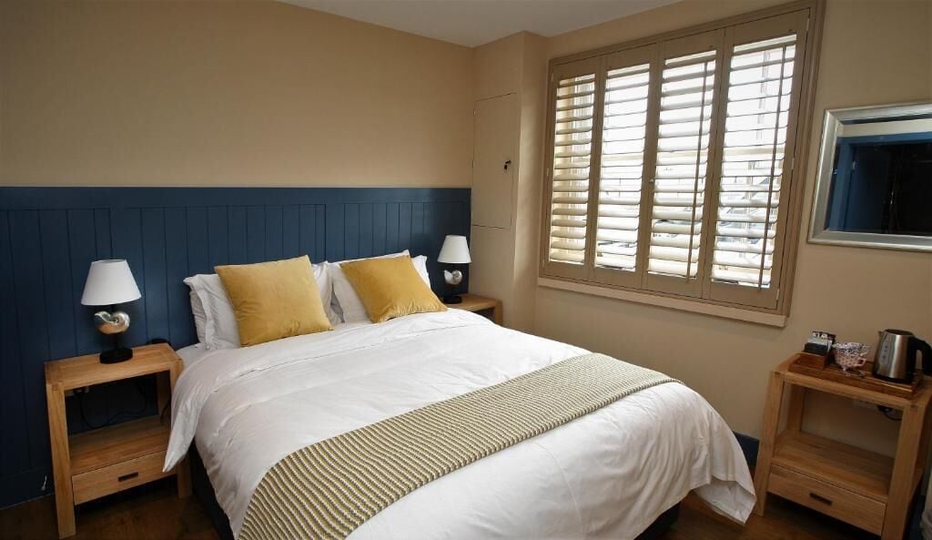 A hotel room with a bed, two bedside tables, a window with blinds, and a wall-mounted TV.