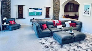 A modern living room with a pool table, leather sofas, and a television displaying a golf game.