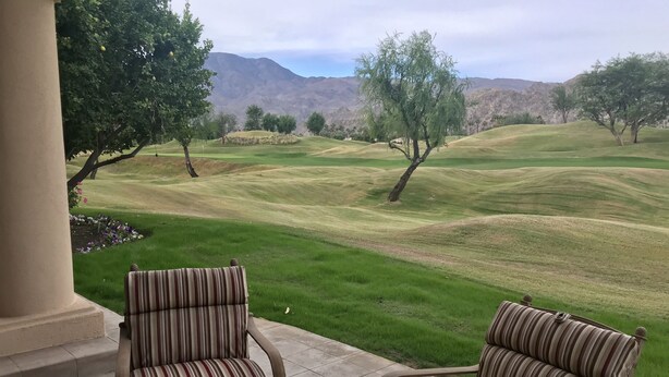 A patio with two striped chairs, a round table, a fire pit, and a plate of fruit and coffee.