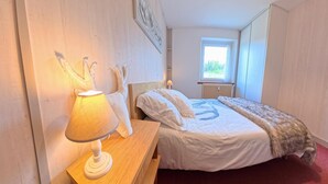 A bedroom with a bed, a bedside table with a lamp, a window, and a radiator. - Marie-Lou's Farm - La Joux Dessus (Prémanon)
