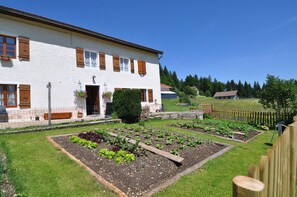 Een wit gebouw met houten luiken en een tuin met verhoogde bakken.
