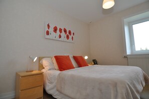 Een slaapkamer met een bed, nachtkastjes, een kunstwerk aan de muur en een raam.