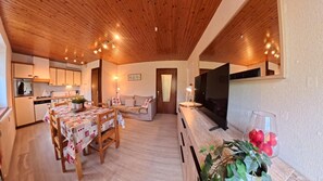 Een gezellig interieur met een houten plafond, een eethoek met een tafel en stoelen, een bank en een keuken met kasten en apparatuur.