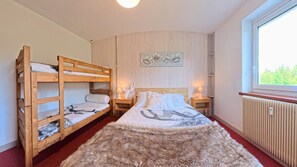 Une pièce avec des lits superposés, un grand lit avec une couverture, un tapis en fourrure, un mur orné d’une œuvre d’art florale, une fenêtre et un radiateur.