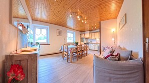 Un intérieur chaleureux avec un plafond en bois, un coin repas et un espace de vie doté d’un canapé.