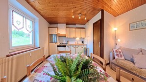 Een gezellig interieur met een houten plafond, een eettafel met een tafelkleed met patroon en een bank met decoratieve kussens.