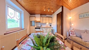 Un intérieur chaleureux avec un plafond en bois, une table à manger recouverte d’une nappe à motifs et un canapé agrémenté de coussins décoratifs.