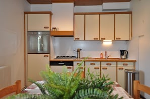 Una cocina compacta con refrigerador, estufa y horno empotrado. Cuenta con gabinetes de madera y una encimera con pileta.
