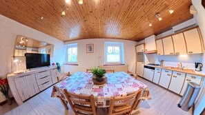 Een gezellige keuken met houten kastjes, een eettafel met een sprei en een televisie.