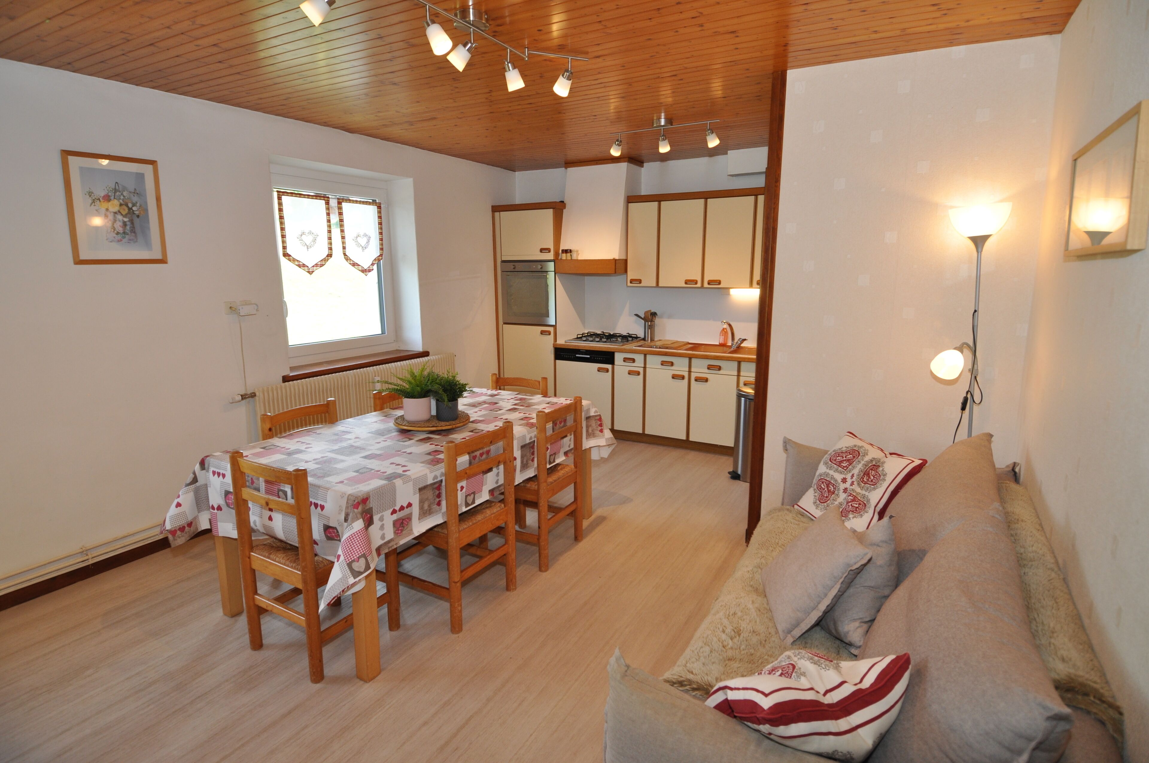 A cozy living room with a wooden ceiling, a dining area with a table and chairs, and a kitchenette with cabinets and a stove.