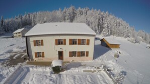 A two-story building with a snow-covered roof and a small attached structure. - Marie-Lou's Farm - La Joux Dessus (Prémanon)
