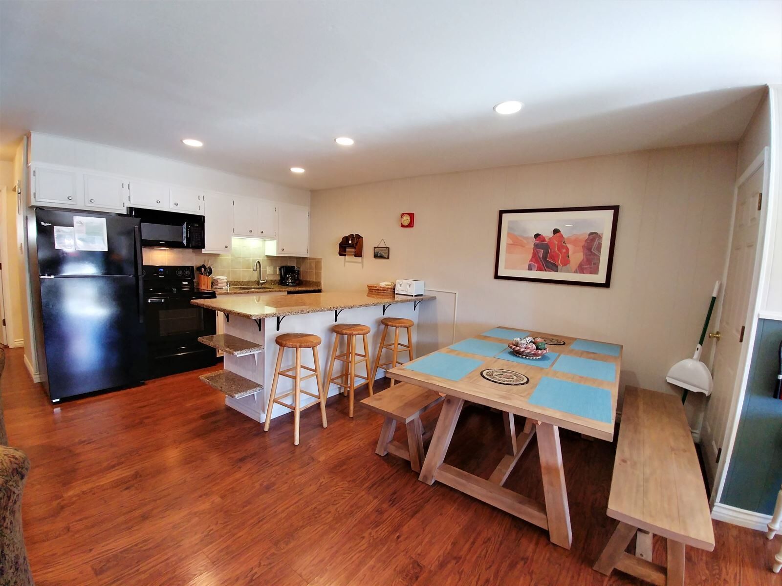 A compact kitchen with a refrigerator, stove, and microwave. There is a dining area with a table and stools.