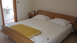 A single bed with a wooden frame, white bedding, and a yellow blanket. There is a nightstand with a lamp and a small table with a glass. A white sink is visible in the background. - Studio apartment in Orebić with Seaview, Terrace, Air condition, WIFI (4669-5) (Orebic)