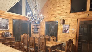 A wooden interior with a dining table and chairs, a chandelier, and a door with a glass panel.