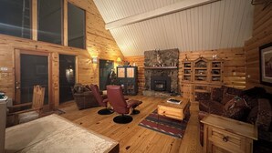 A cozy log cabin interior with a fireplace, wooden furniture, and a stone wall.