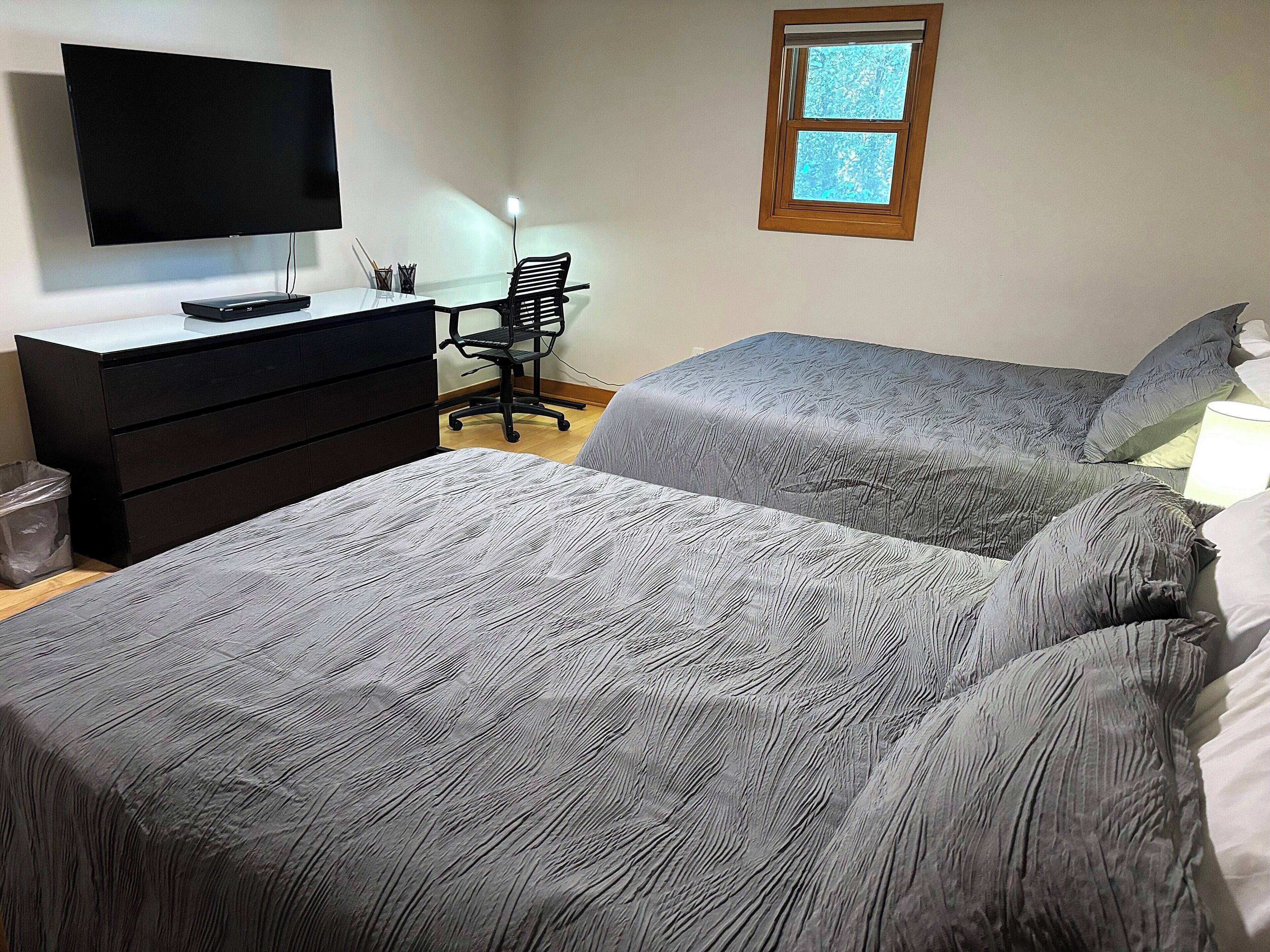 Un dormitorio con dos camas, un escritorio, una silla, un televisor y una ventana.