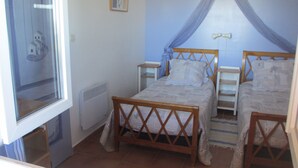 Un dormitorio con dos camas de madera, una ventana, un radiador y un cuadro en la pared.