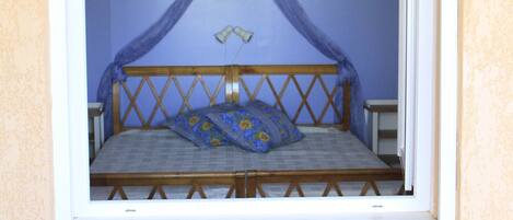Una habitación con una cama debajo de una ventana, una mesita y una silla.