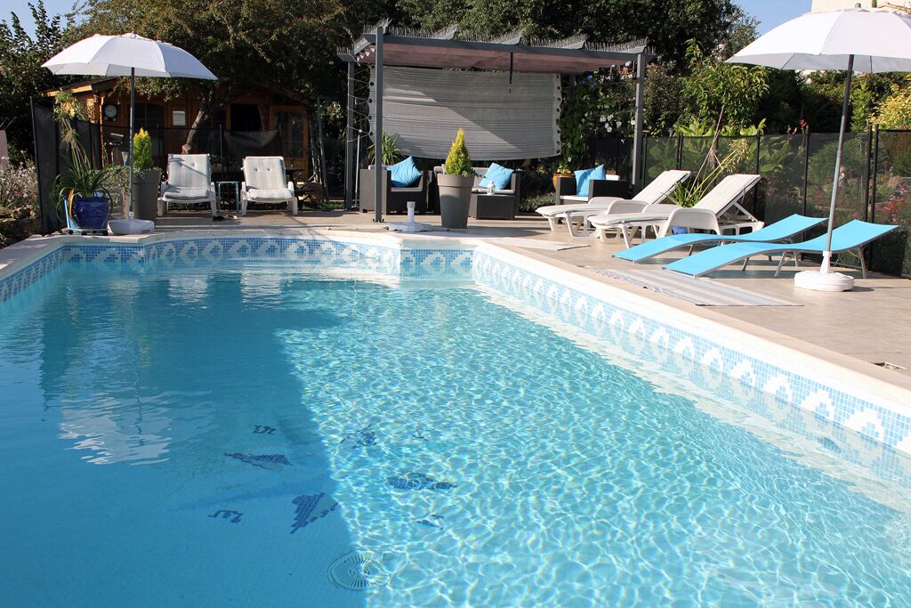 Piscina cristalina con sillas de descanso y sombrillas, rodeada de follaje.