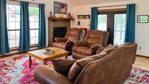A living room with leather armchairs, a wooden coffee table, a fireplace, and a large window with curtains. - Maggie May @ Tenkiller - 2 minutes to boat ramp & state park! (Vian)
