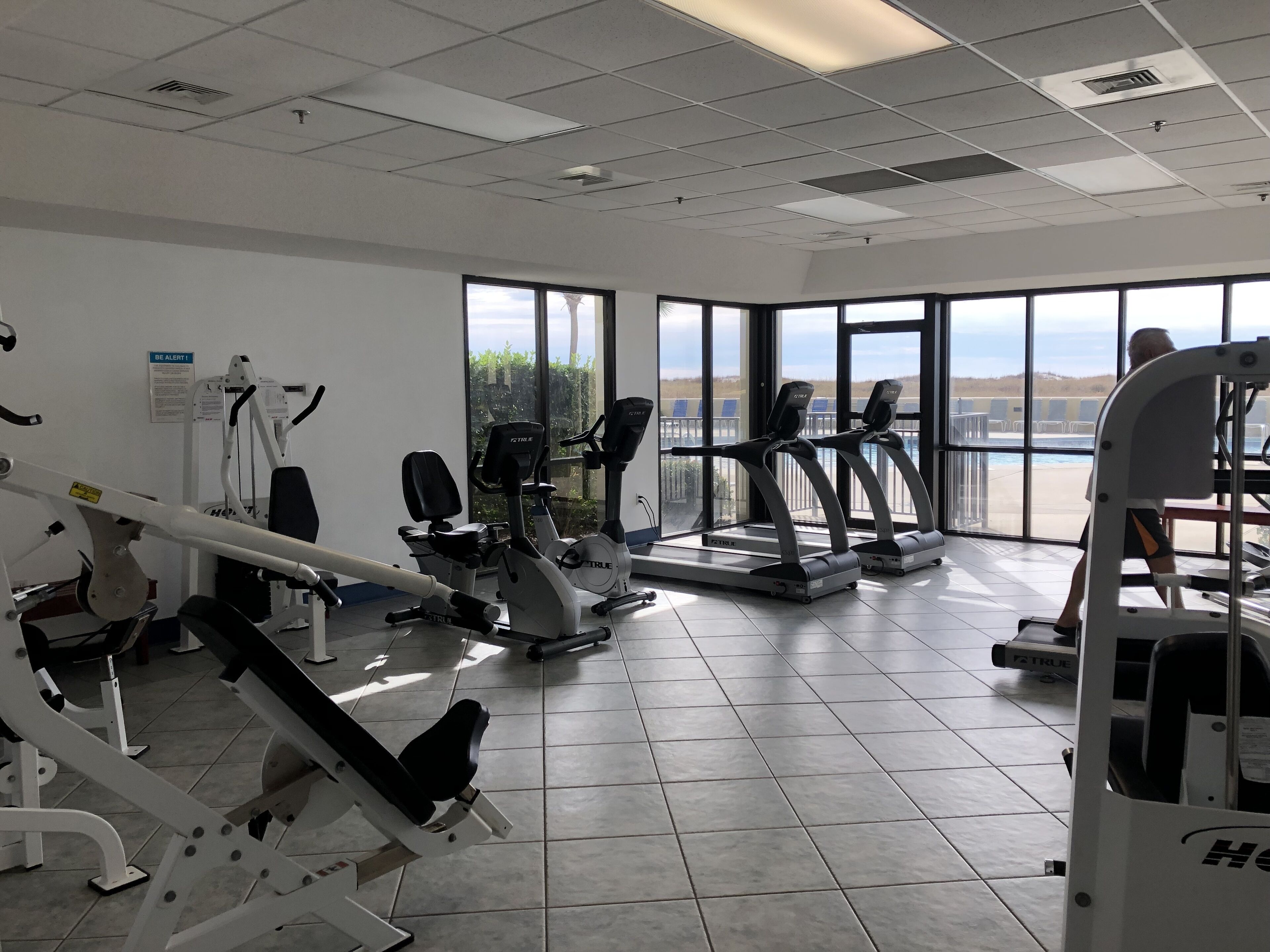 Une salle de sport équipée de divers appareils d’exercice, dotée de grandes fenêtres et offrant une vue sur l’extérieur.