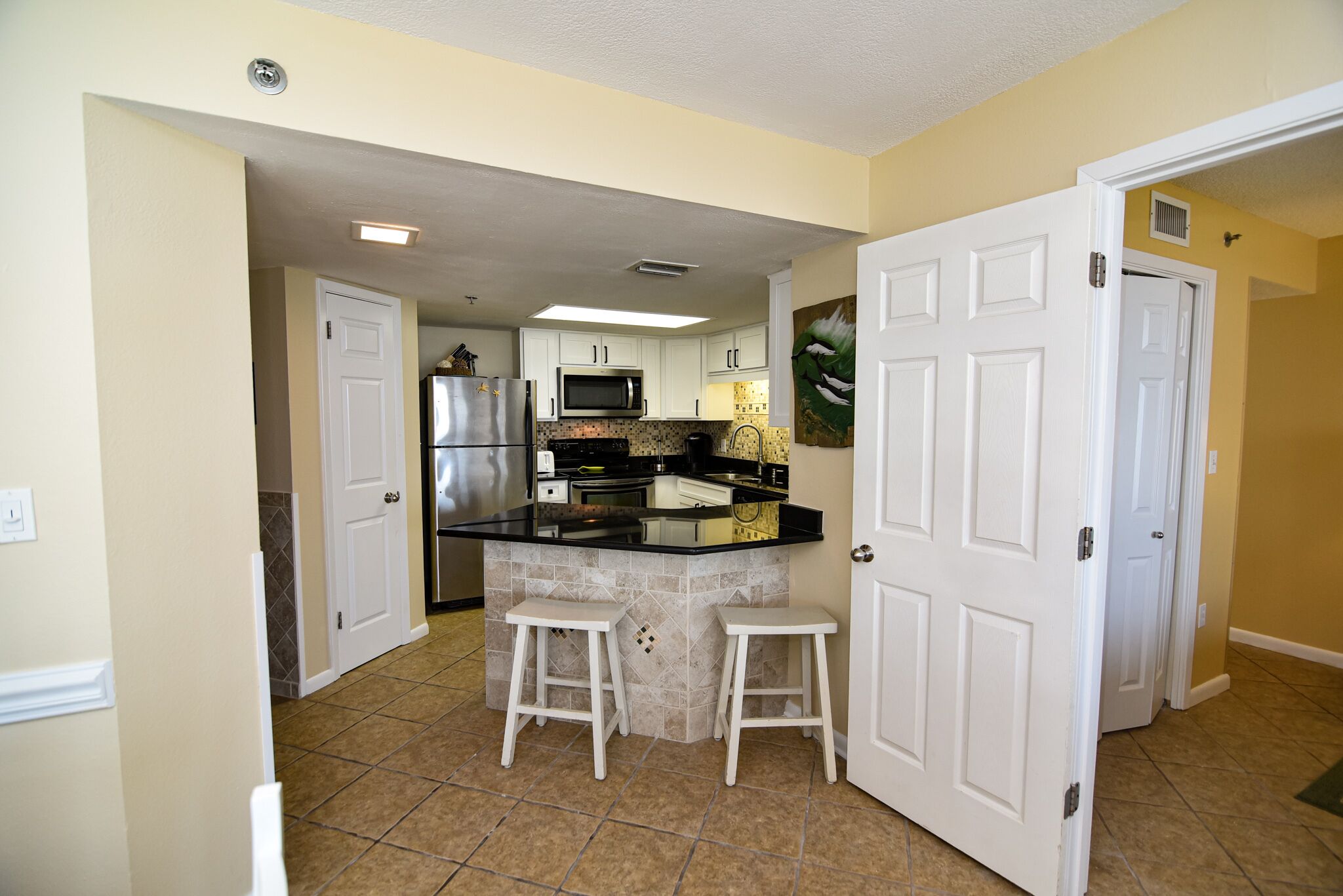 A kitchen with white cabinets, a black countertop, and two white stools.