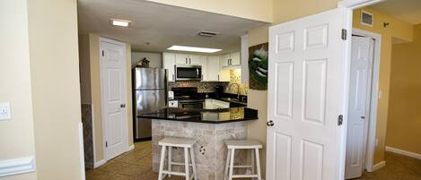 A kitchen with white cabinets, a black countertop, and two white stools.
