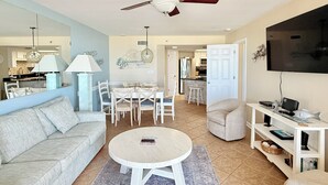 A living room with a sofa, coffee table, and TV stand. There is a dining area with chairs and a table. A ceiling fan is visible. - Phoenix VI #606 - Resort Style complex owner's Beach Chairs Included in Rental (Orange Beach)