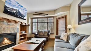 A living room with a fireplace, a large window, a sofa, and a coffee table. - Sundial 1 BR in Canyons Village, private patio, outdoor pool and hot tubs, walk to hiking and biking (Park City)