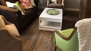 Una sala de estar con un sofá marrón, un sillón verde, una mesa de centro blanca y un aparador de madera.