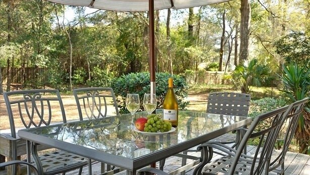 Un espacio de comedor al aire libre con una mesa de vidrio, sillas de metal y una botella de vino.