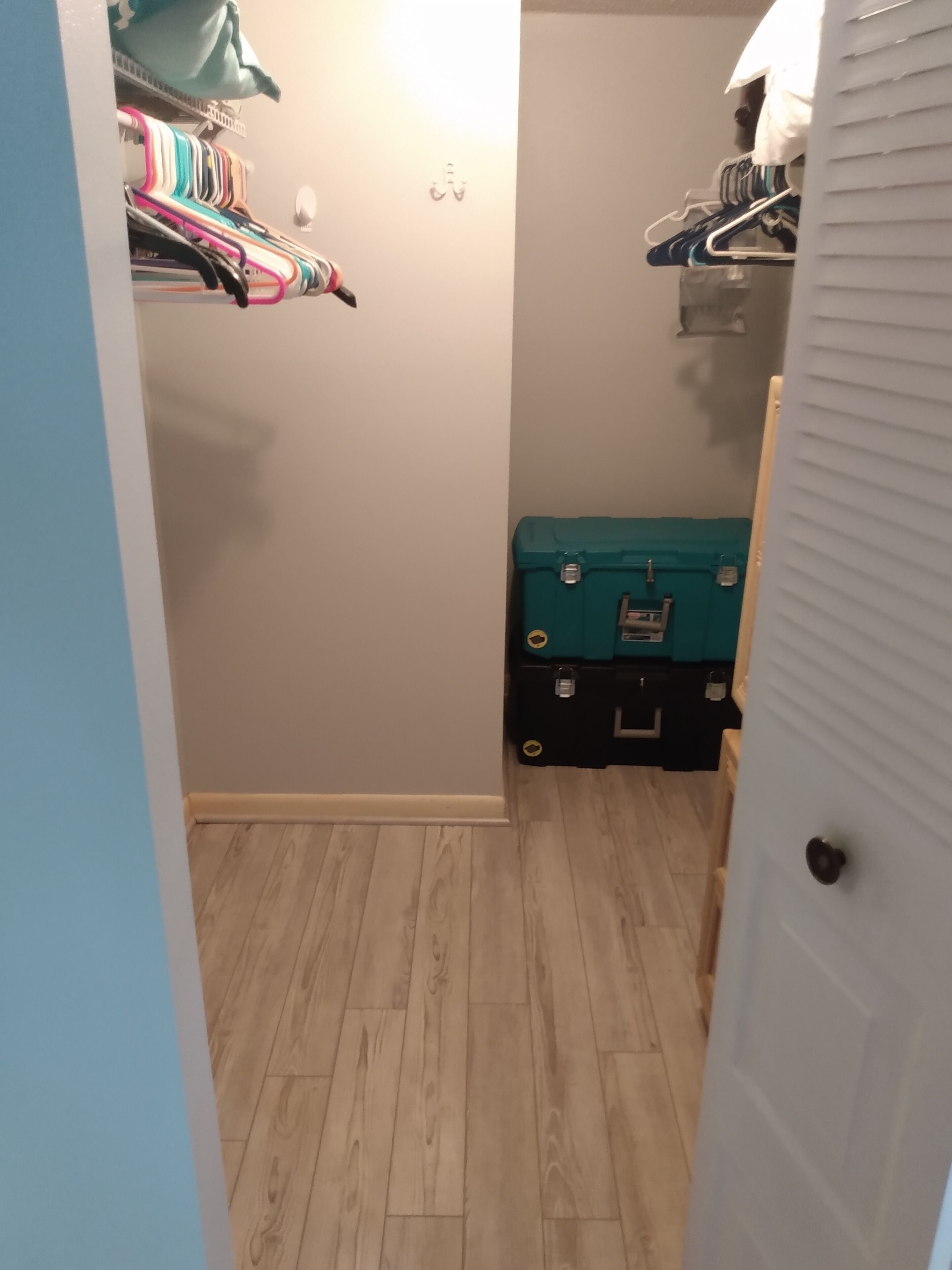 Ein schmaler Flur mit einem Schrank links, der Kleidung und eine türkisblaue Aufbewahrungsbox enthält.