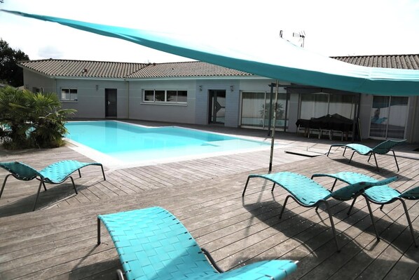 Uma área à beira da piscina com um deck de madeira, espreguiçadeiras e um espaço de estar coberto.