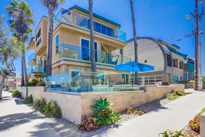 A modern multi-story building with a glass facade, outdoor seating area, and palm trees.