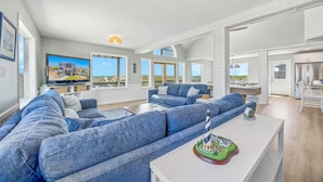 A spacious living area with a large sofa, a coffee table with a decorative item, and a television displaying a scenic view.