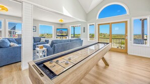 A spacious living room with a foosball table, large windows, and a view of the beach.