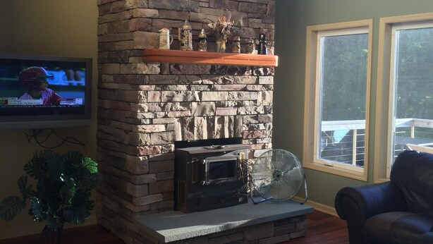 A living room with a stone fireplace, a television, a fan, and a leather couch. - Deruyter lake waterfront  (Deruyter)