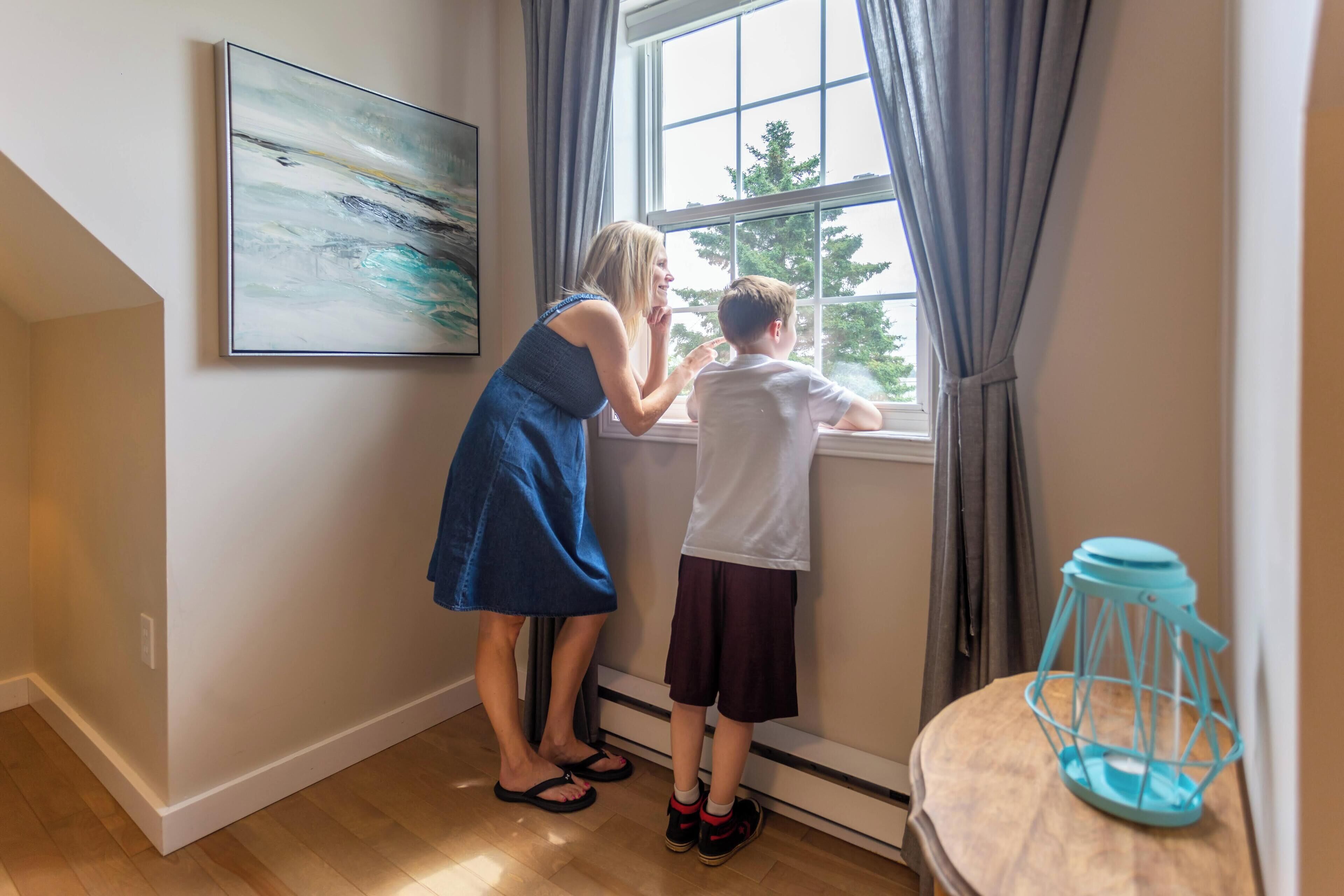 A room with a large window, a painting on the wall, and a blue lantern on a wooden table.