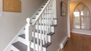 A staircase with white balusters and dark steps, a 'Welcome' anchor sign, and a window with a gothic arch design. - Adventure Awaits at Salt & Tide Ocean Retreat (Hubbards)
